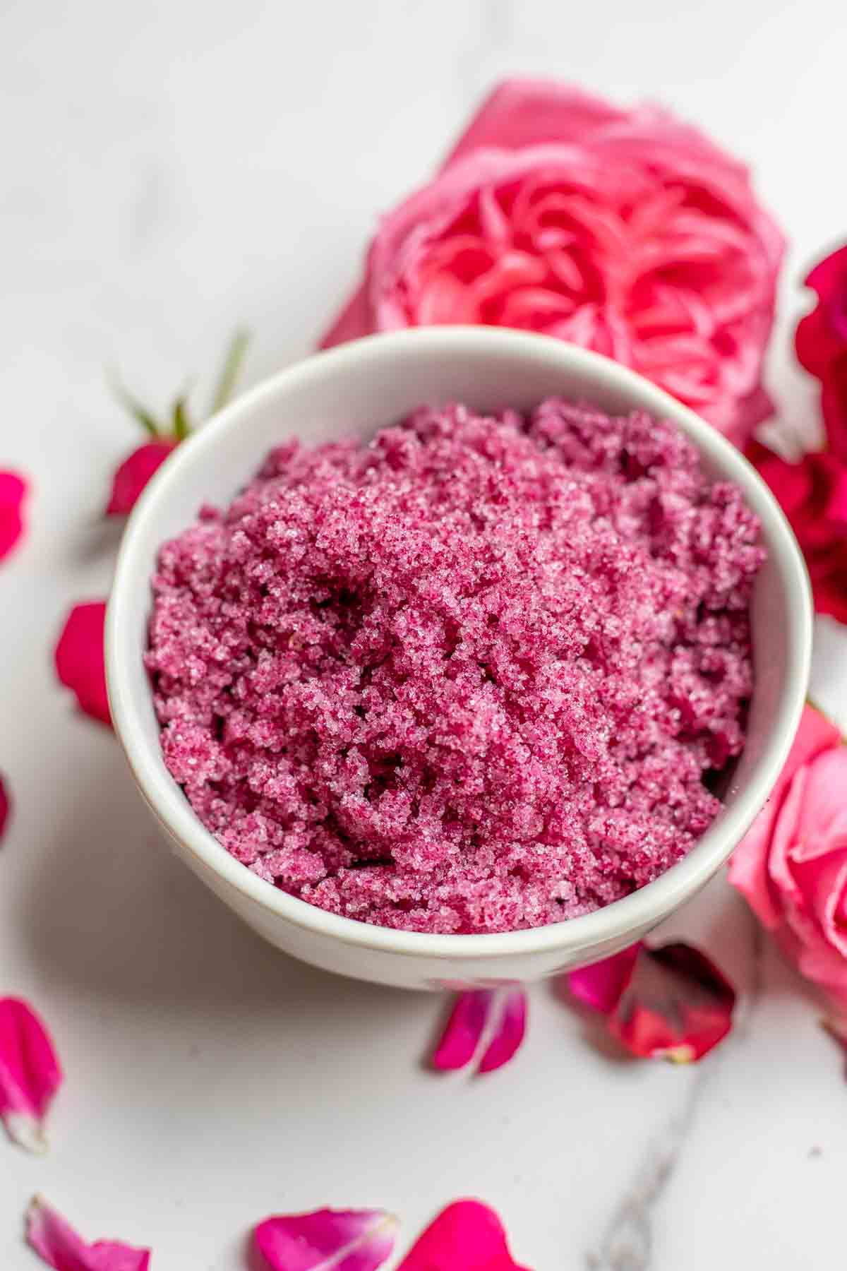 A bowl of beautiful pink rose sugar surrounded by pink and red roses.