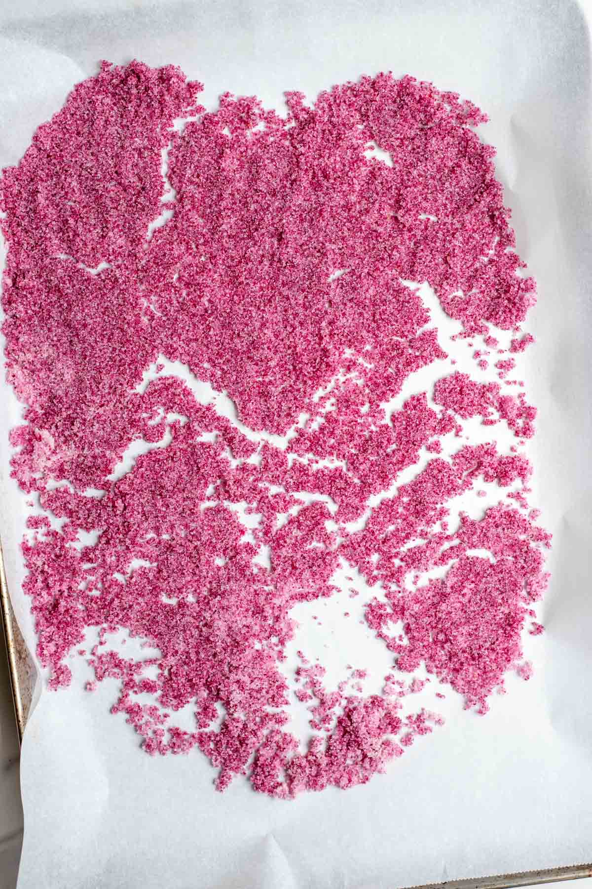 Rose sugar spread out on a parchment lined baking sheet to dry.