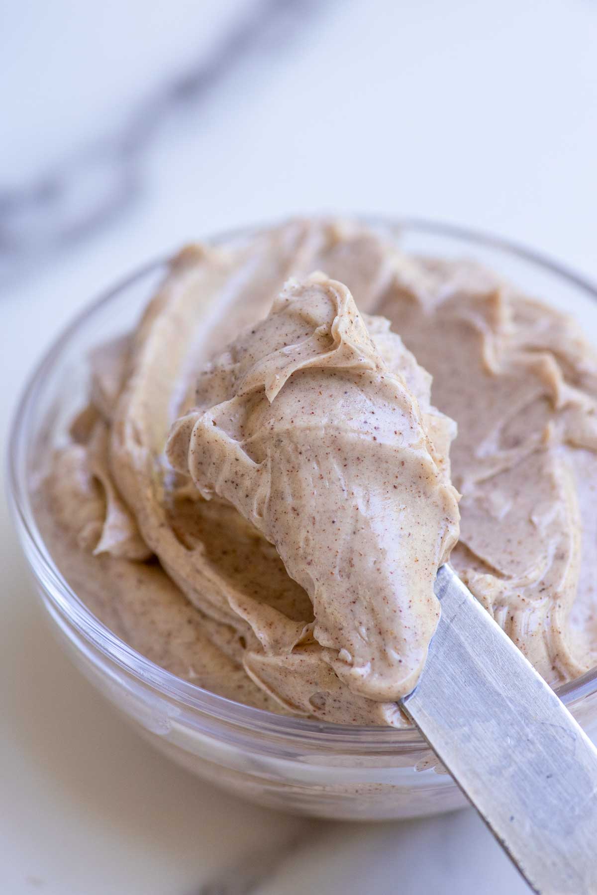 A knife with a scoopful of cinnamon honey butter coming out of a glass bowl.
