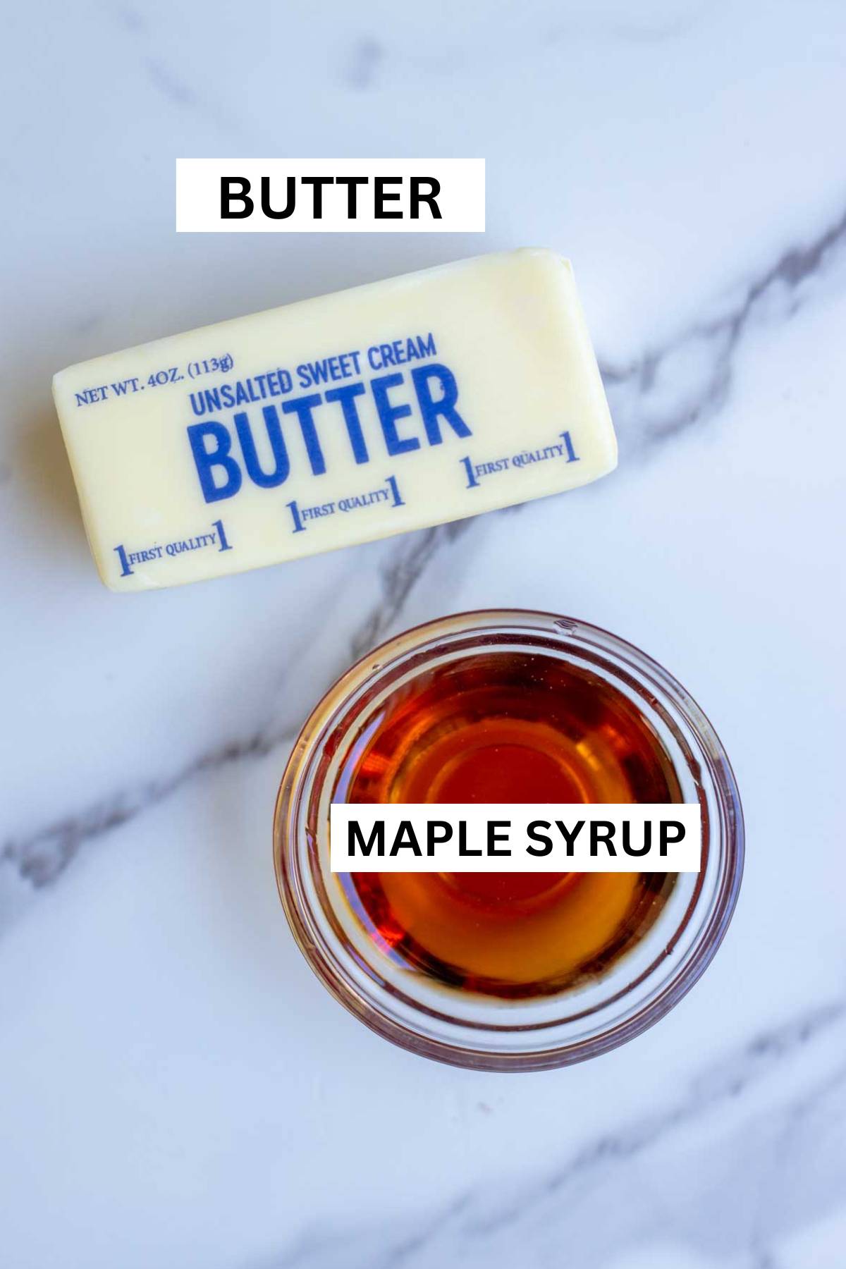 A stick of butter and little bowl of maple syrup on a countertop.