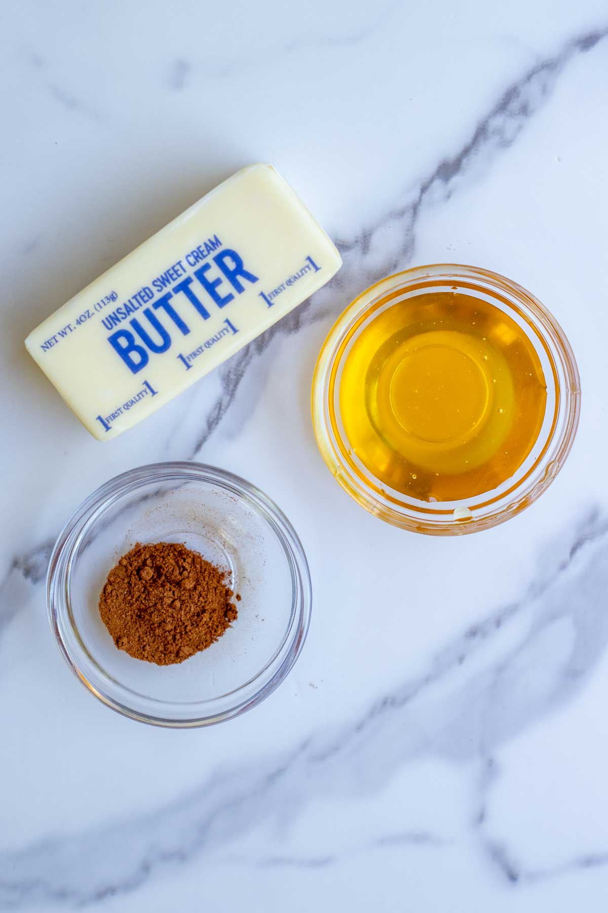 Stick of butter and two glass bowls of cinnamon and honey on a countertop.