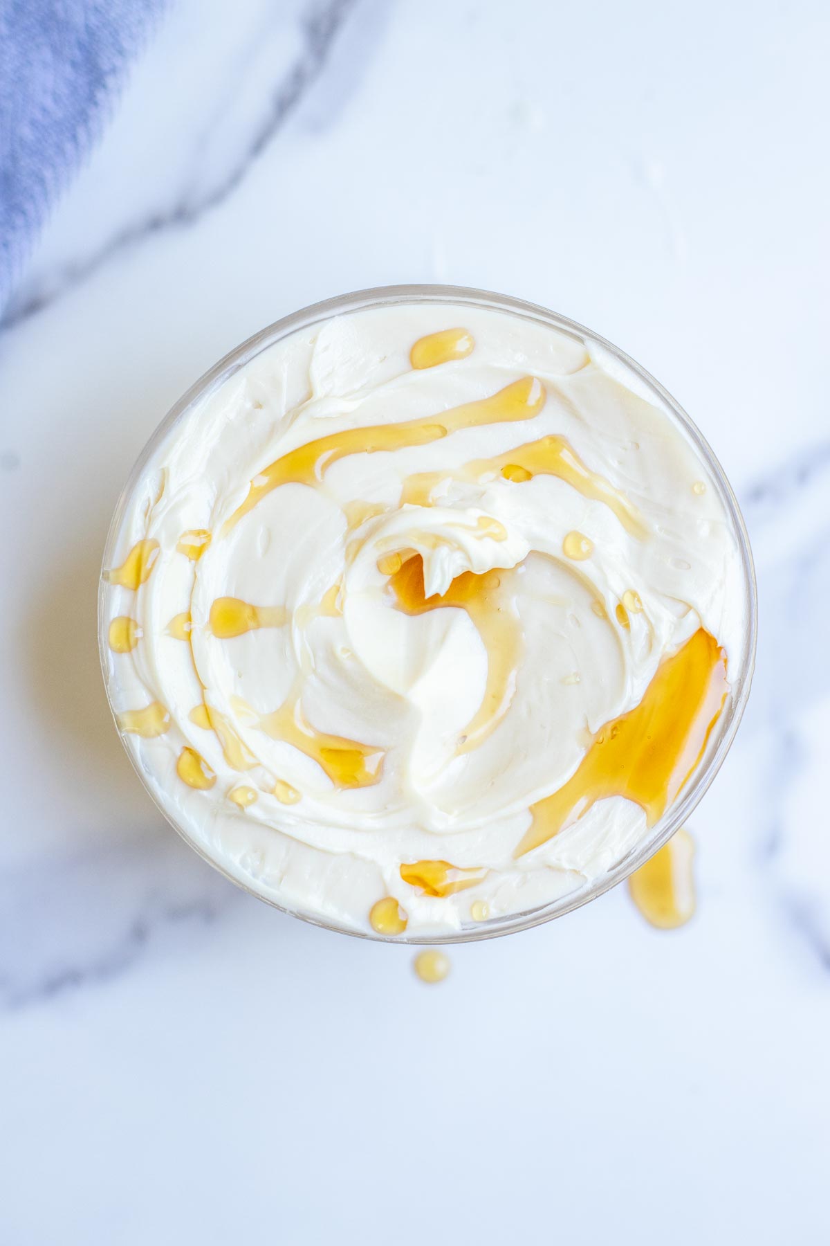 Overhead photo of maple butter topped with a little extra maple syrup in a glass bowl on a countertop.