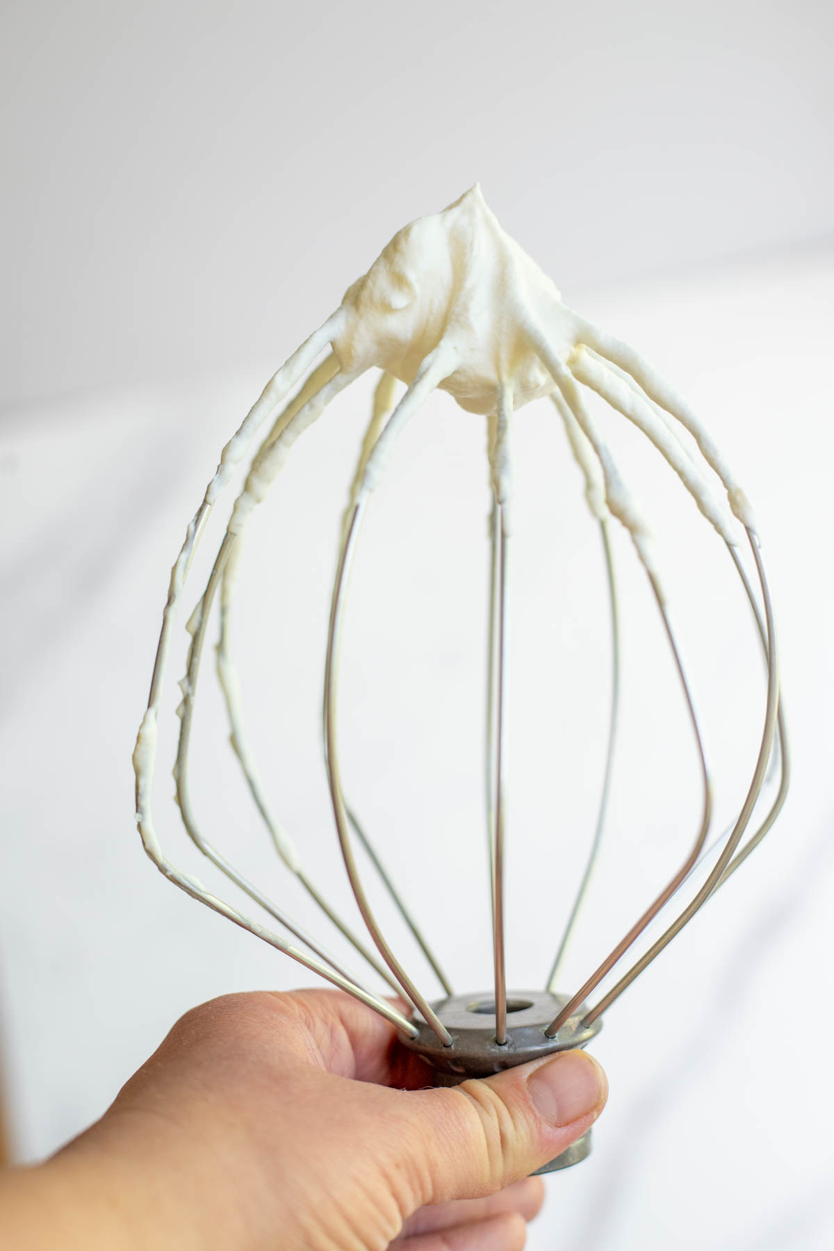 Hand holding a whisk attachment with a dollop of maple whipped cream on the top.