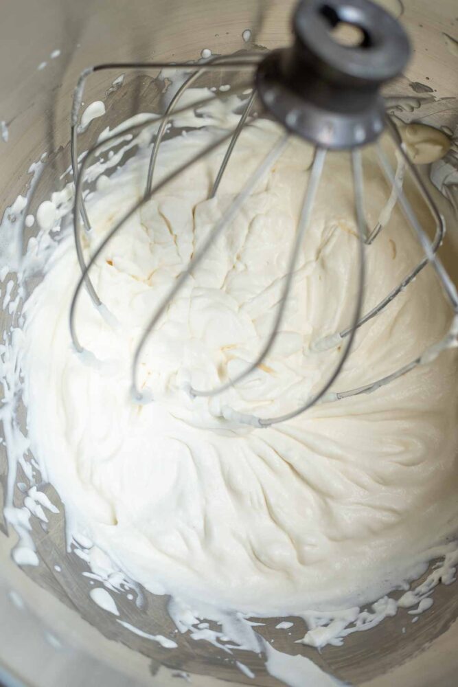 Whipped cream in a stand mixer bowl with whisk attachment.