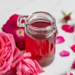 Rose syrup in a small glass jar surrounded by pink and red roses.