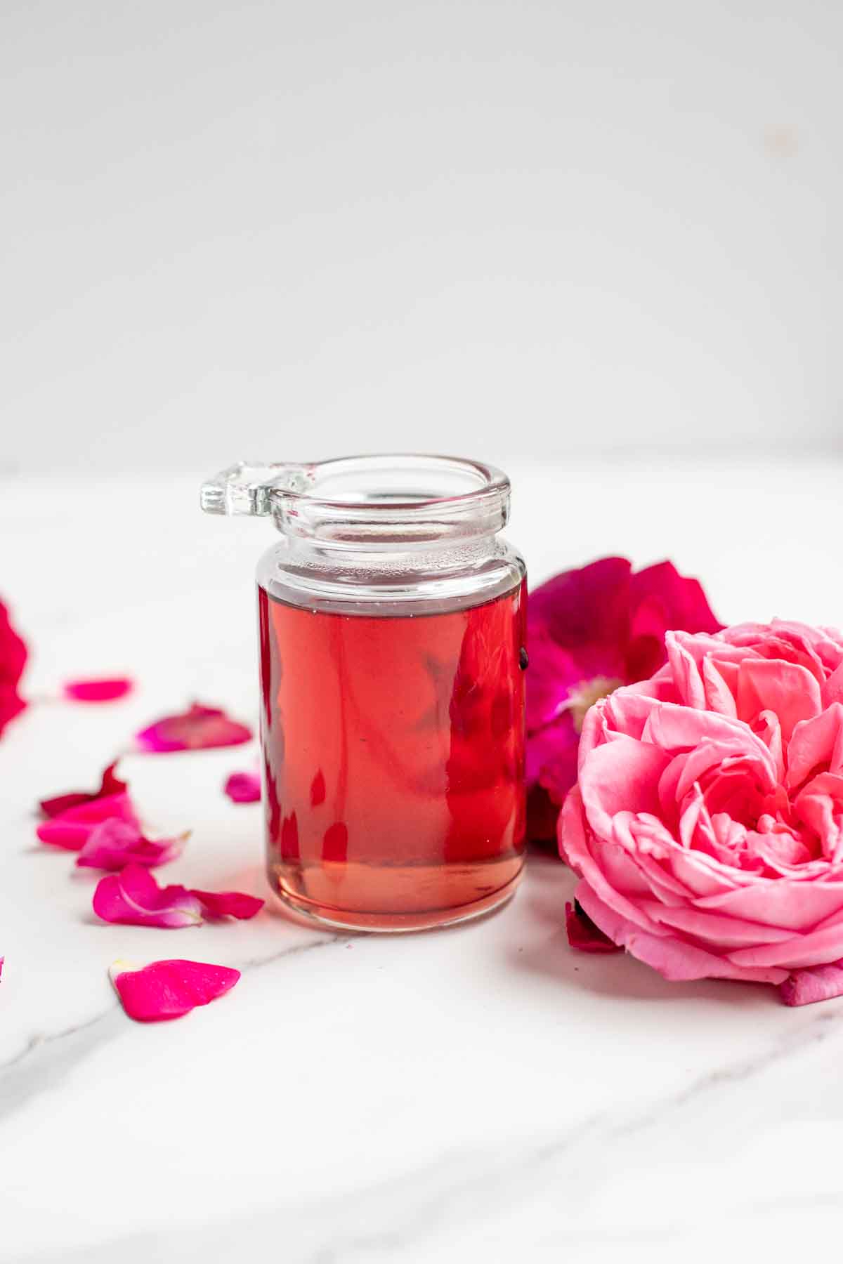 Rose simple syrup in a glass jar surrounded by roses and rose petals.