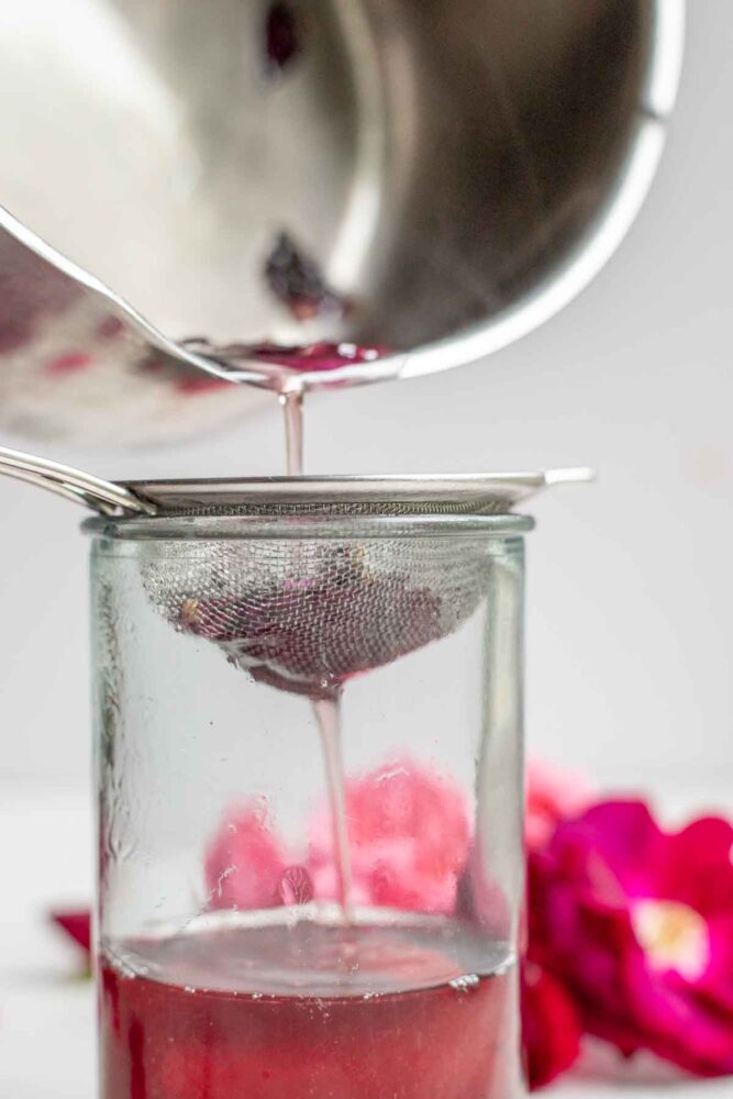 Straining rose syrup into a glass jar.
