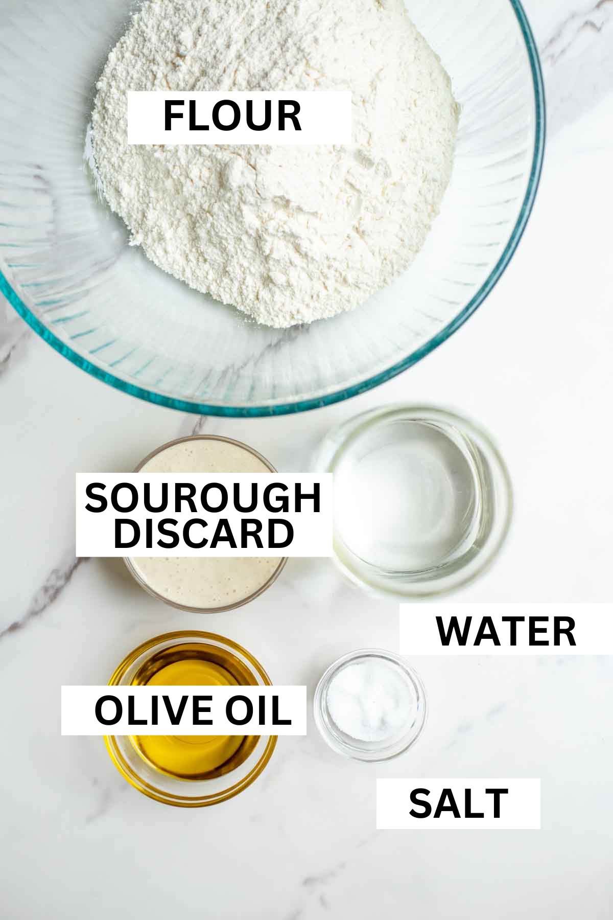 Glas bowls of flour sourdough starter, olive oil, water and salt on a countertop.