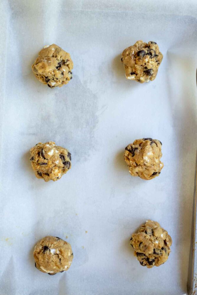 Cookie dough balls on a parchment lined baking sheet.