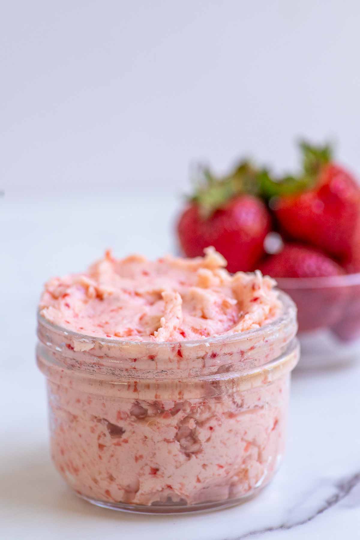 Strawberry butter in a glass jar with a bowl of strawberries in the background.