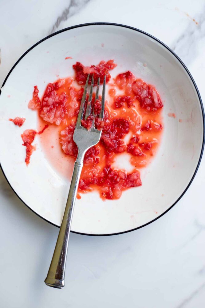 Mashed strawberries in a bowl with a fork.