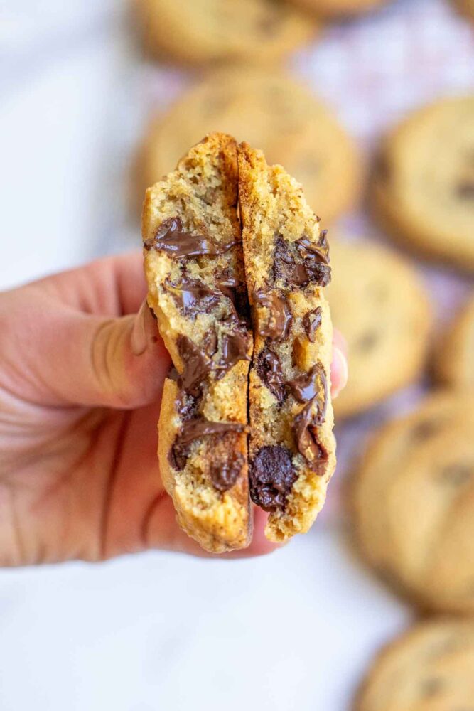 Thick and gooey browned butter sourdough chocolate chip cookies cut in half being help in a hand to show how thick and gooey the cookies are.