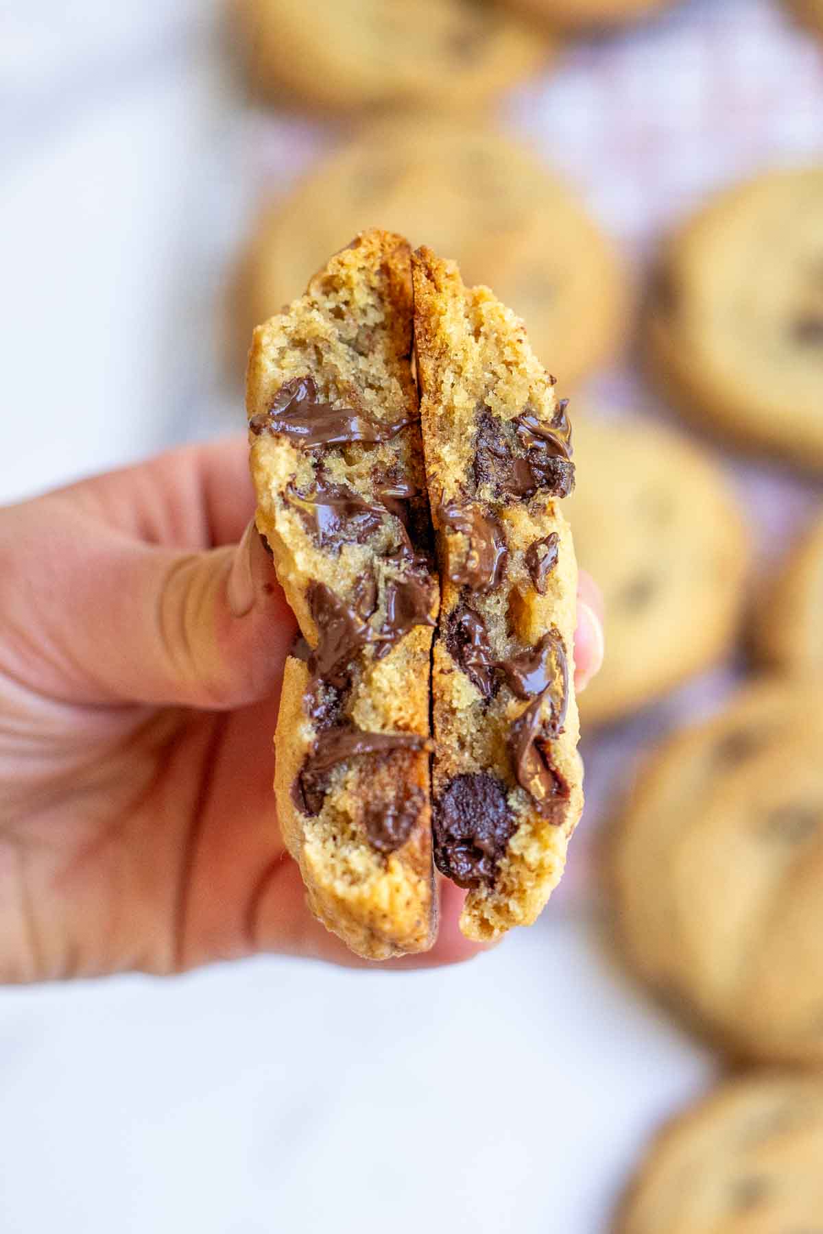 Thick and gooey browned butter sourdough chocolate chip cookies cut in half being help in a hand to show how thick and gooey the cookies are.