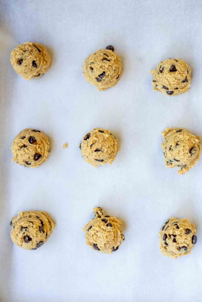 Cookie dough scooped onto a parchment lined baking sheet.