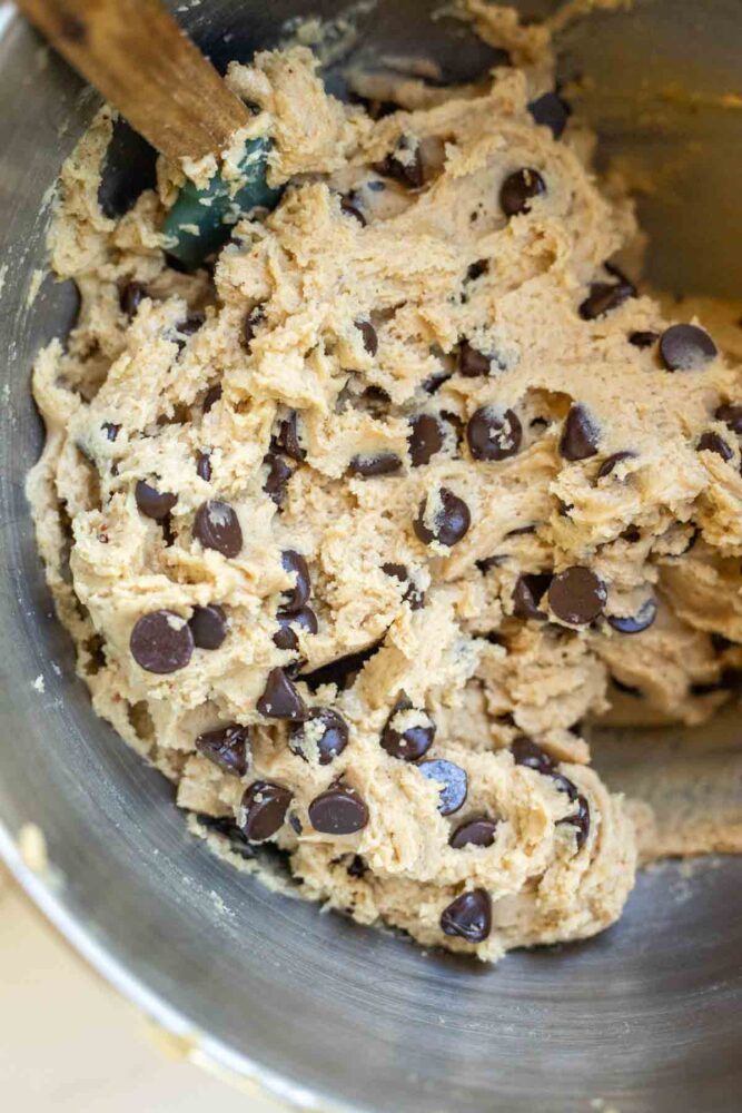 Chocolate chips added to cookie dough in a stand mixer bowl.