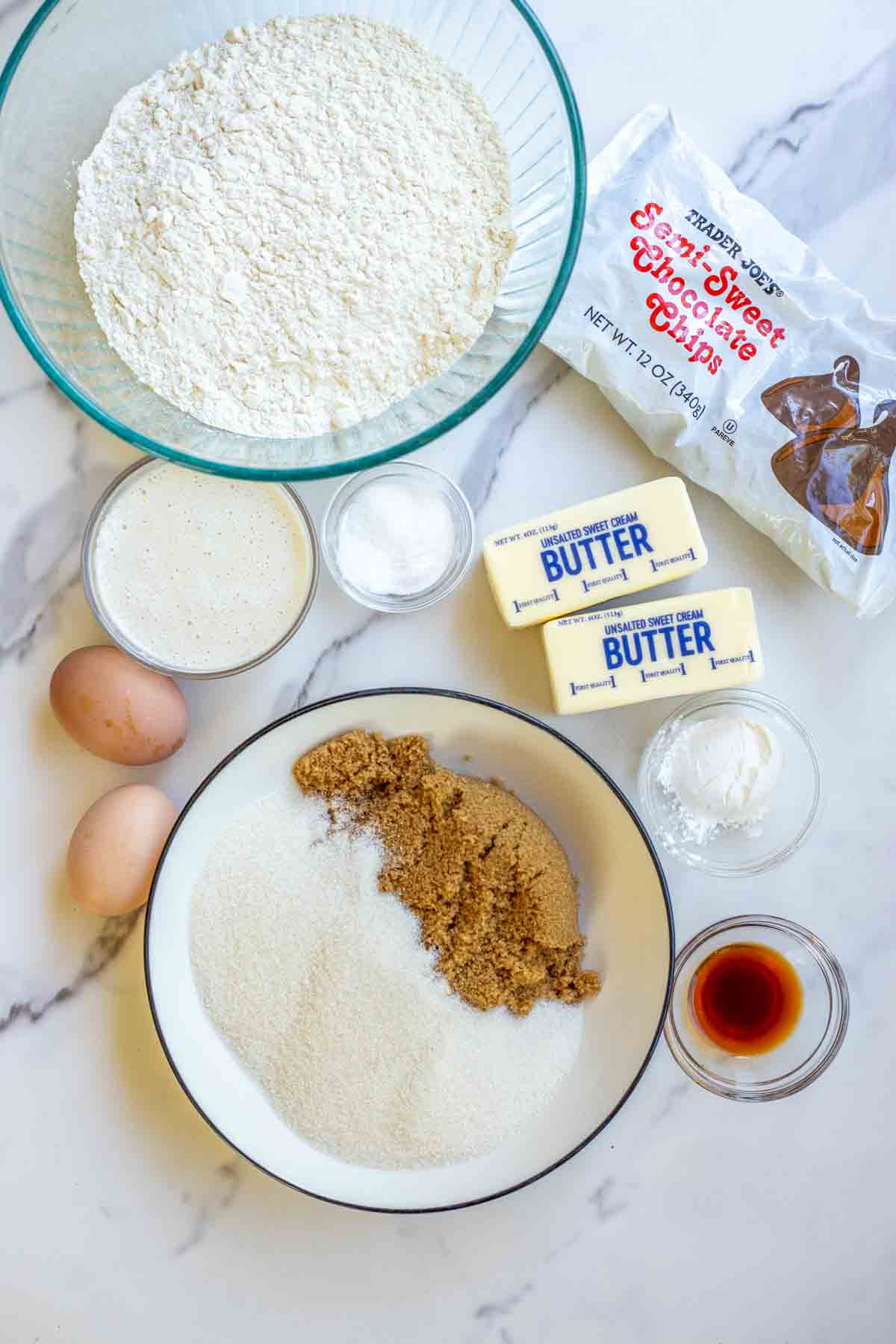 bowls of sugar, flour, sourdough starter, vanilla extract and more on a countertop.