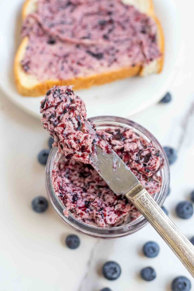 knife full of blueberry butter balancing on a jar with toast in the background.