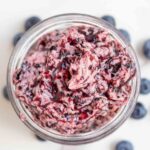 Overhead photo blueberry butter in a jar surrounded by more blueberries.