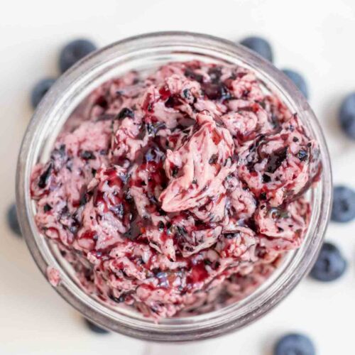 Overhead photo blueberry butter in a jar surrounded by more blueberries.