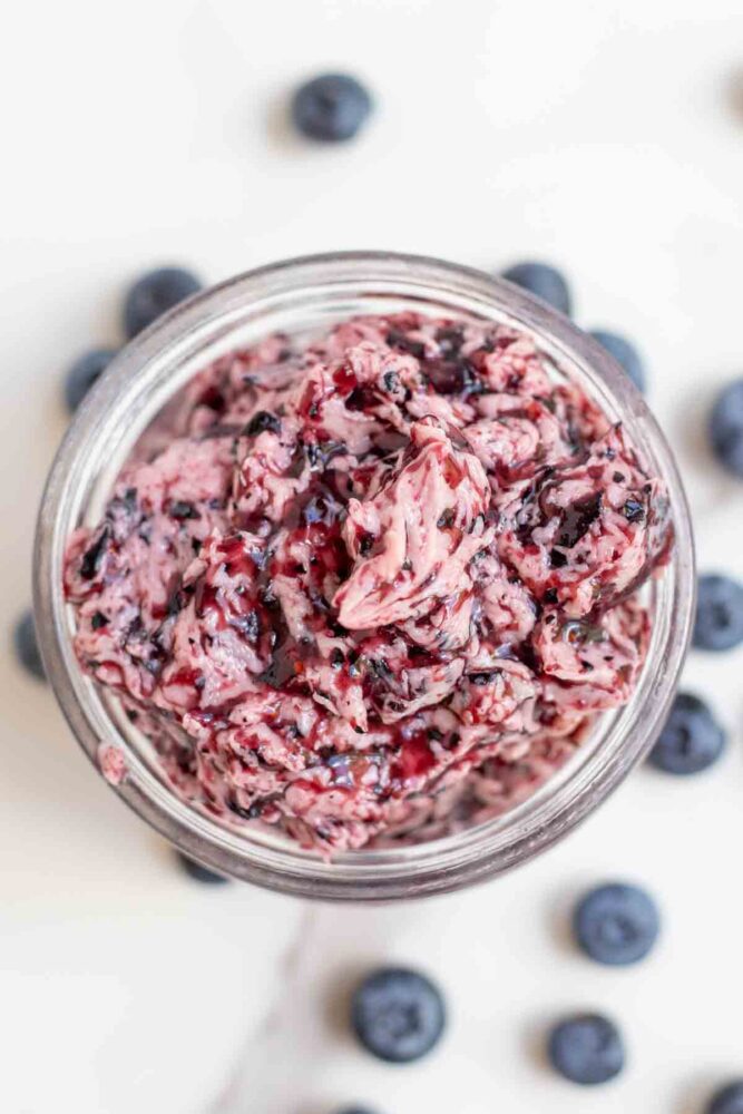 Overhead photo blueberry butter in a jar surrounded by more blueberries.