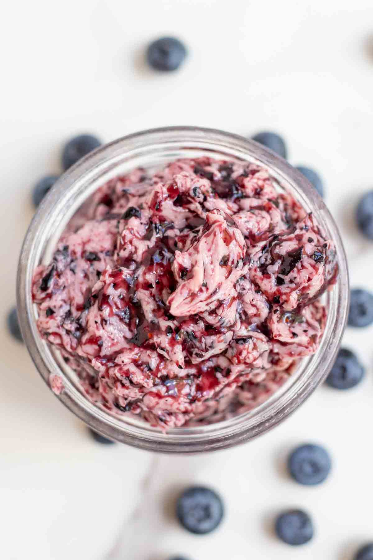 Overhead photo blueberry butter in a jar surrounded by more blueberries.