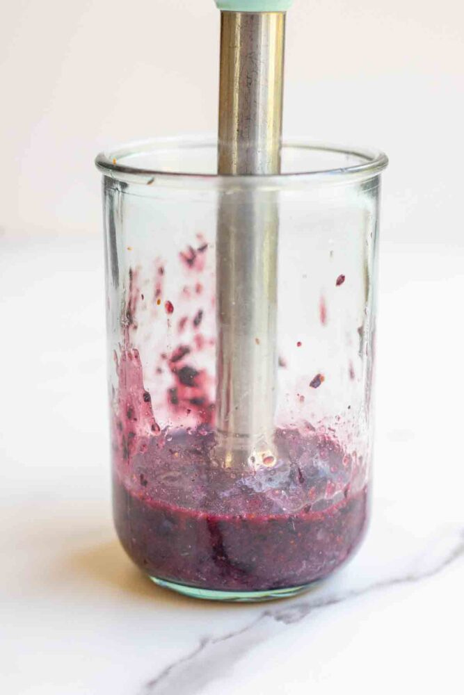 blueberries being blended in a glass with an immersion blender.