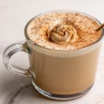 Maple latte topped with whipped cream and cinnamon in a glass mug.
