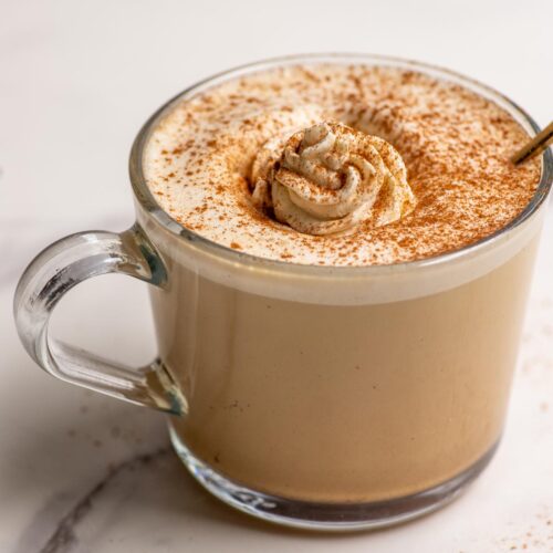 Maple latte topped with whipped cream and cinnamon in a glass mug.