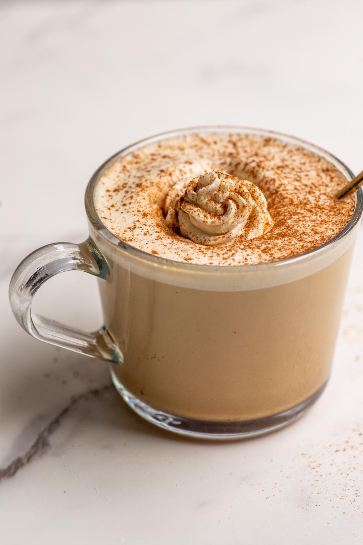 Maple latte topped with whipped cream and cinnamon in a glass mug.