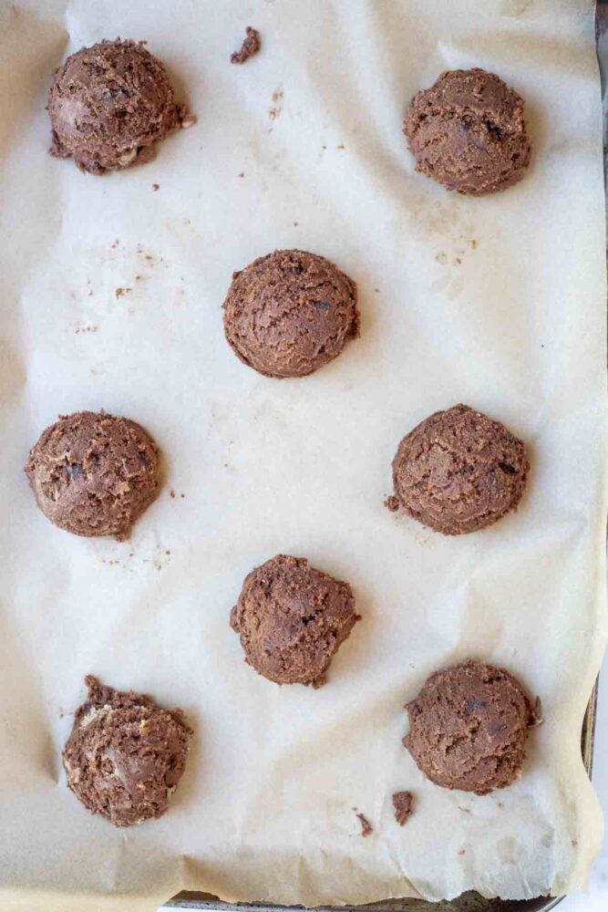Double chocolate sourdough cookie dough scooped out onto a parchment lined baking sheet.