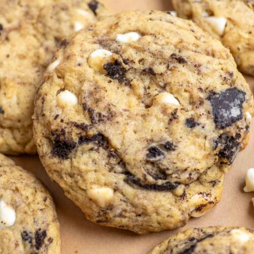 Close up picture of sourdough cookies and cream cookies with chunks of white chocolate and cookie pieces spread out on parchment paper.