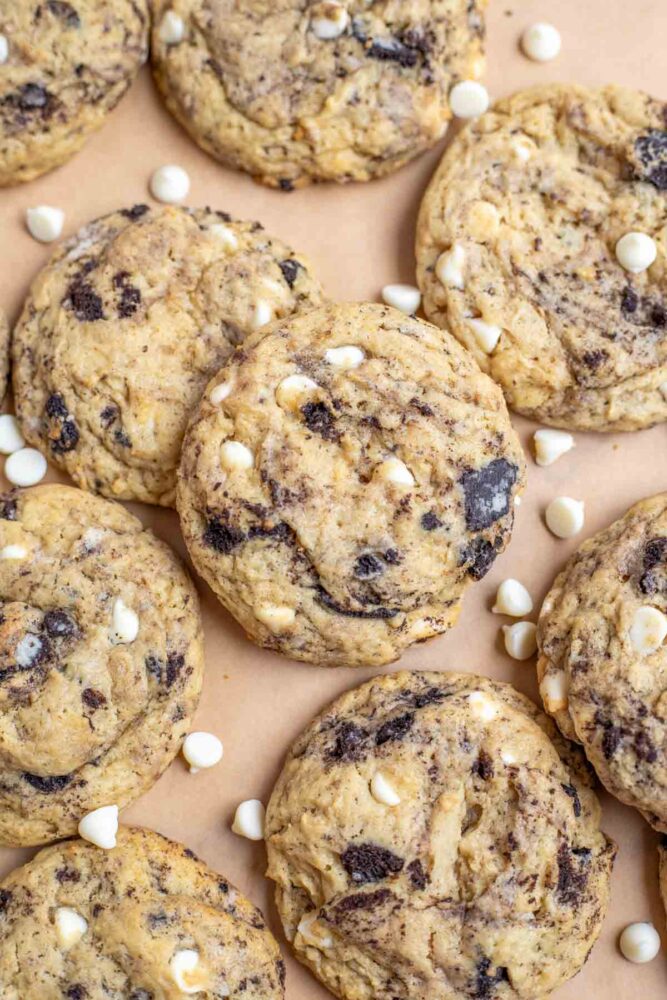 Sourdough cookies and cream cookies spread out on parchment paper and sprinkled with extra white chocolate chips.