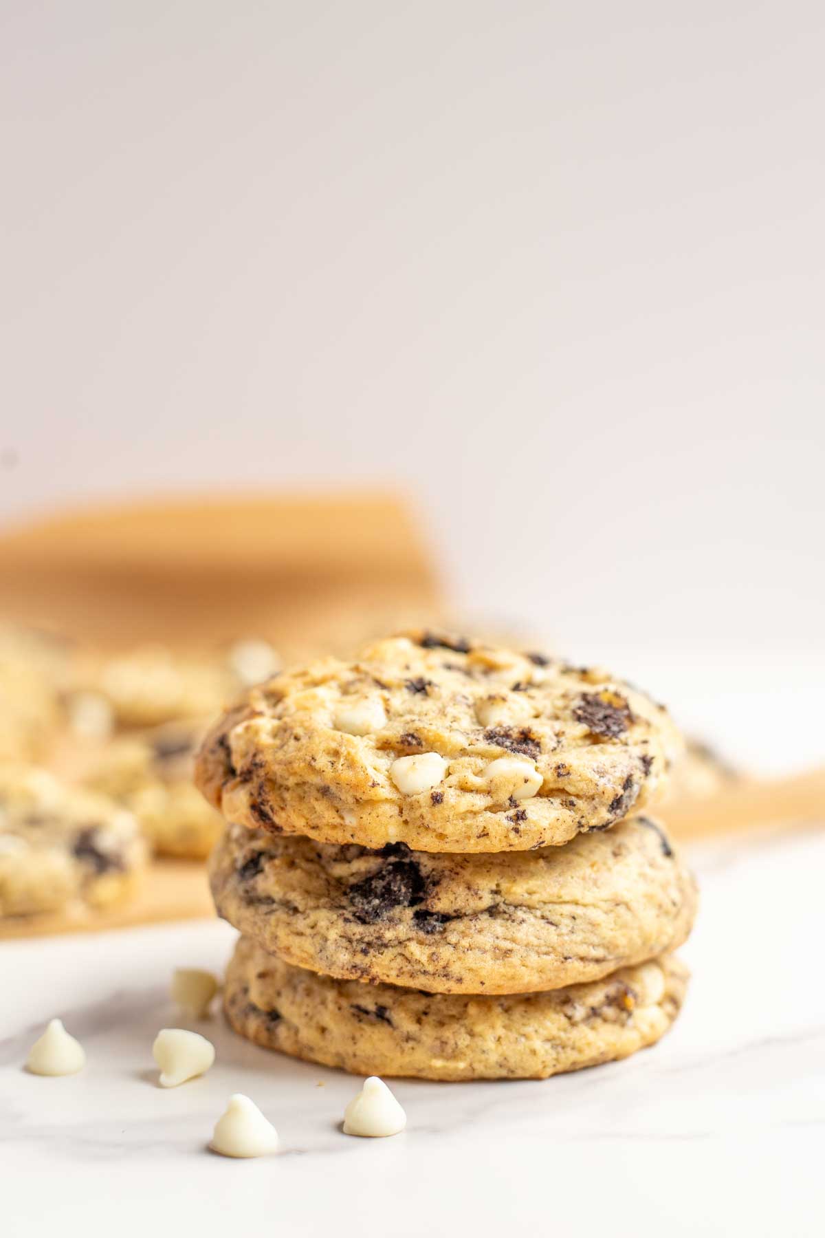 Sourdough cookies and cream cookies stacked up 3 high with white chocolate chips around the cookies.