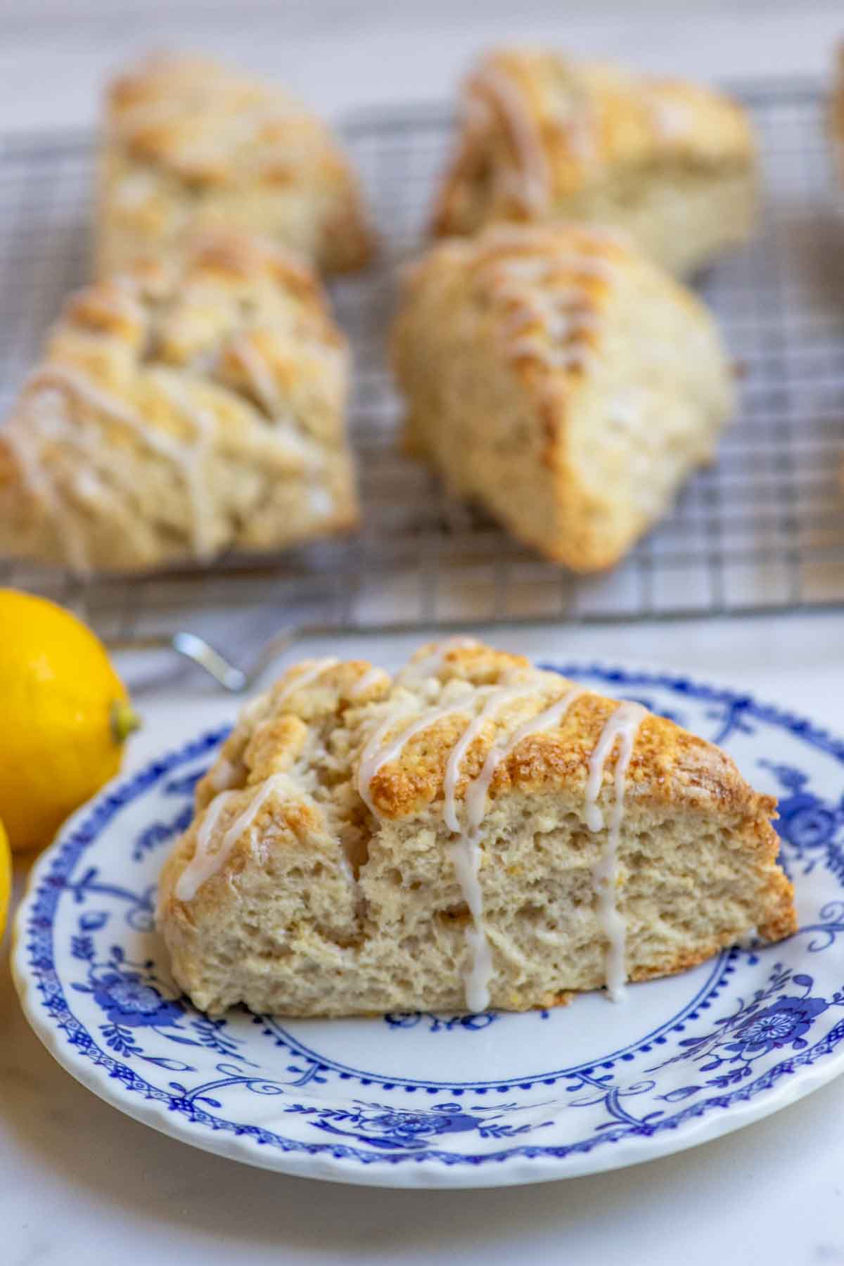 Sourdough lemon scones drizzled with lemon icing on a blue and white vintage plate with more scones in the background.
