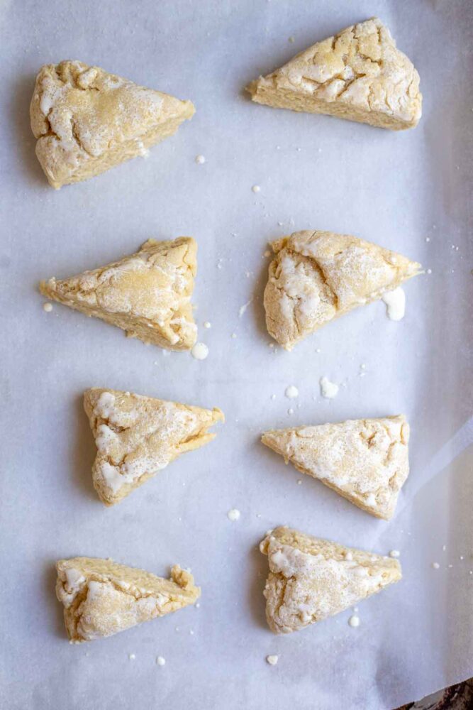 Scone dough on parchment paper topped with cream.