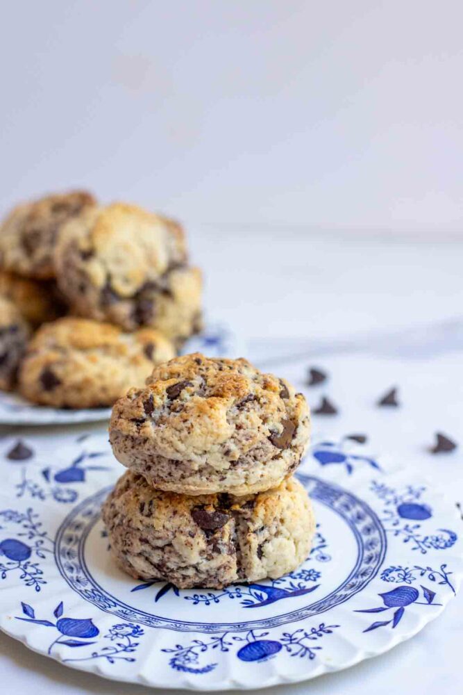 two sourdough chocolate chip scones stacked on a blue and white plate with more scones in the background.