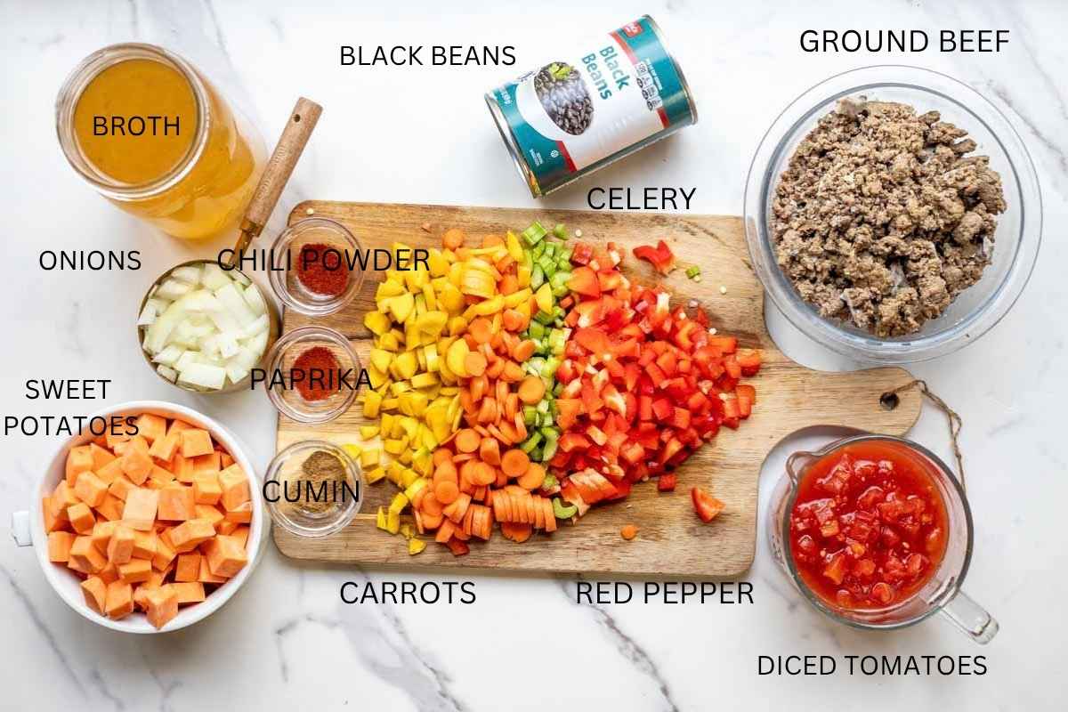 cutting board with chopped vegetables, bowls of ground beef, canned tomatoes, sweet potatoes, broth and other items on a countertop.