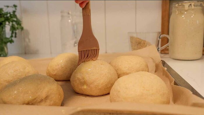 Brushing whole wheat burger buns with an egg wash.