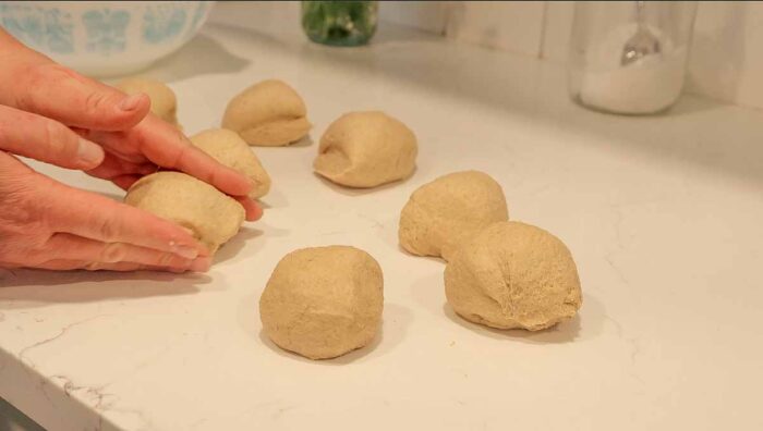 Dividing and shaping whole wheat burger buns on a countertop.