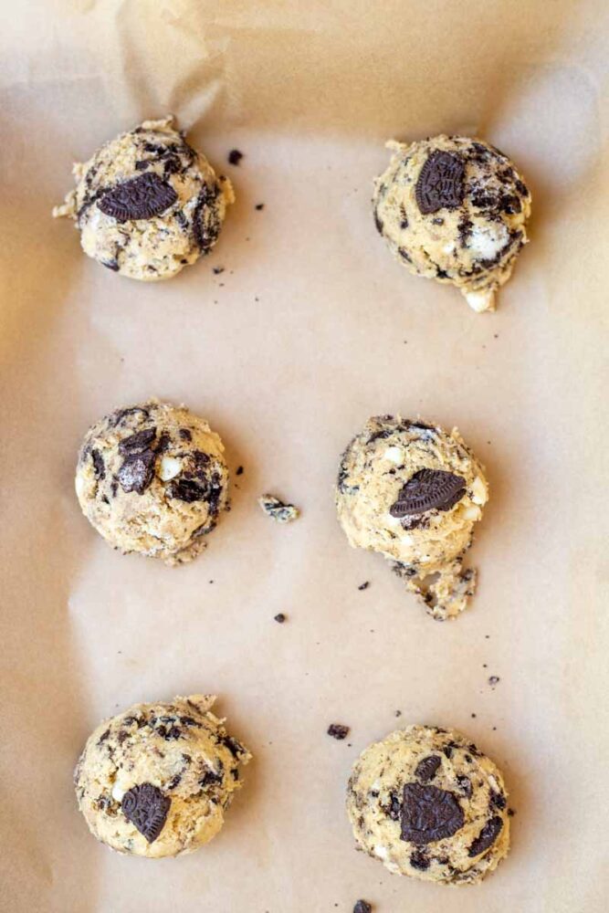 Cookie dough balls topped with extra chocolate cookies on parchment lined baking sheet.