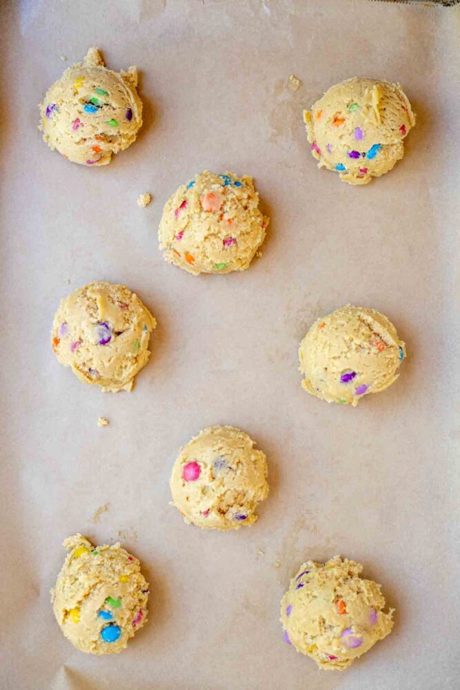 scooped sourdough m&m cookies on parchment paper lined baking sheet.
