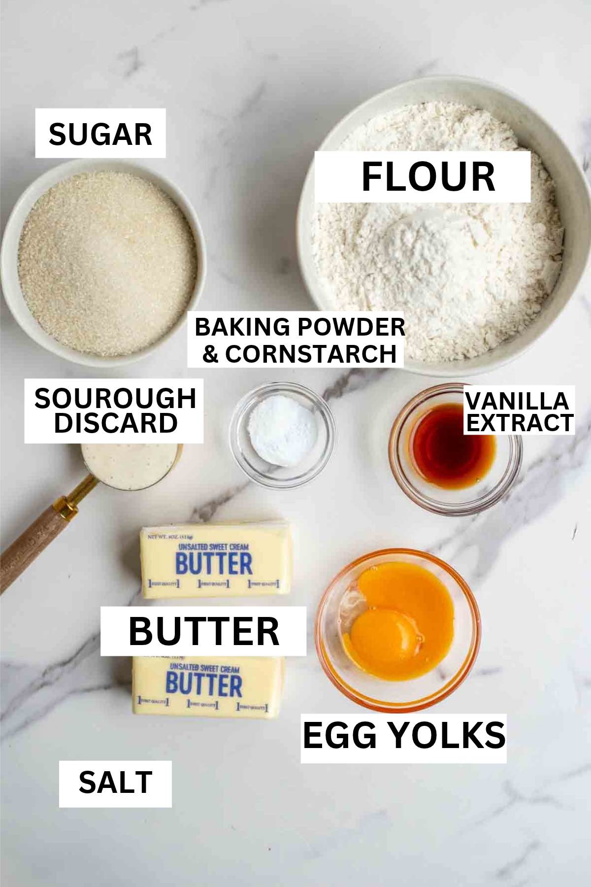 Bowls of flour, sugar, vanilla extract, and more on a countertop.
