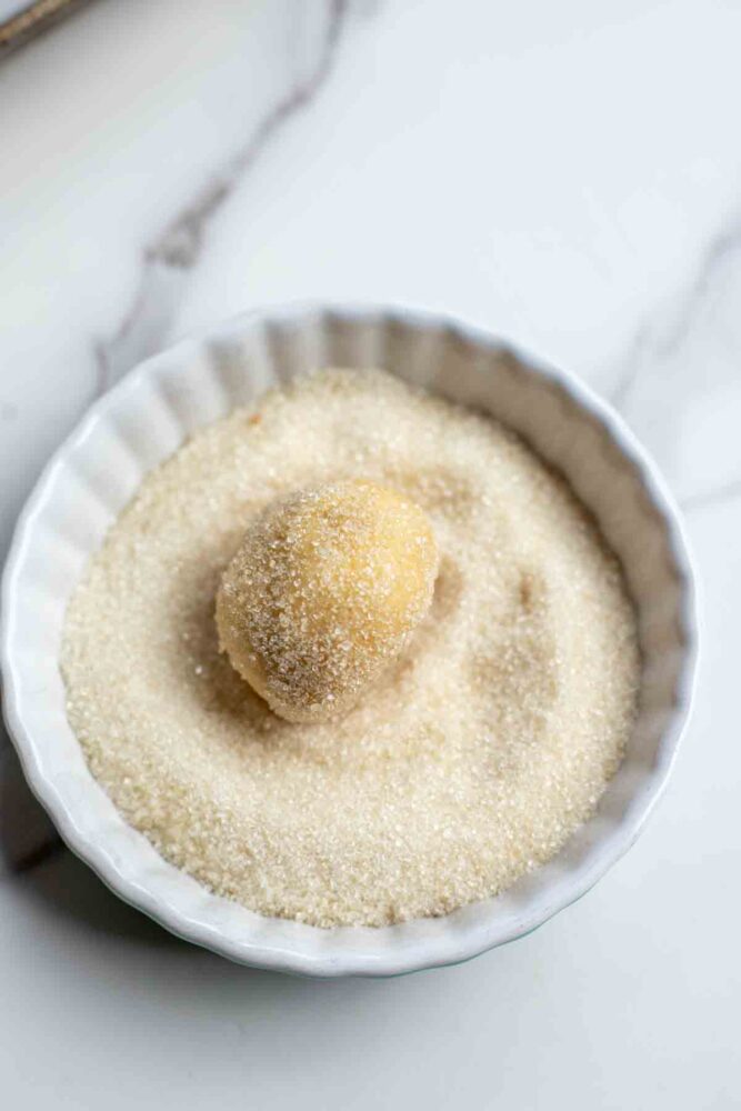 Rolling sugar cookie dough in sugar in a small bowl.